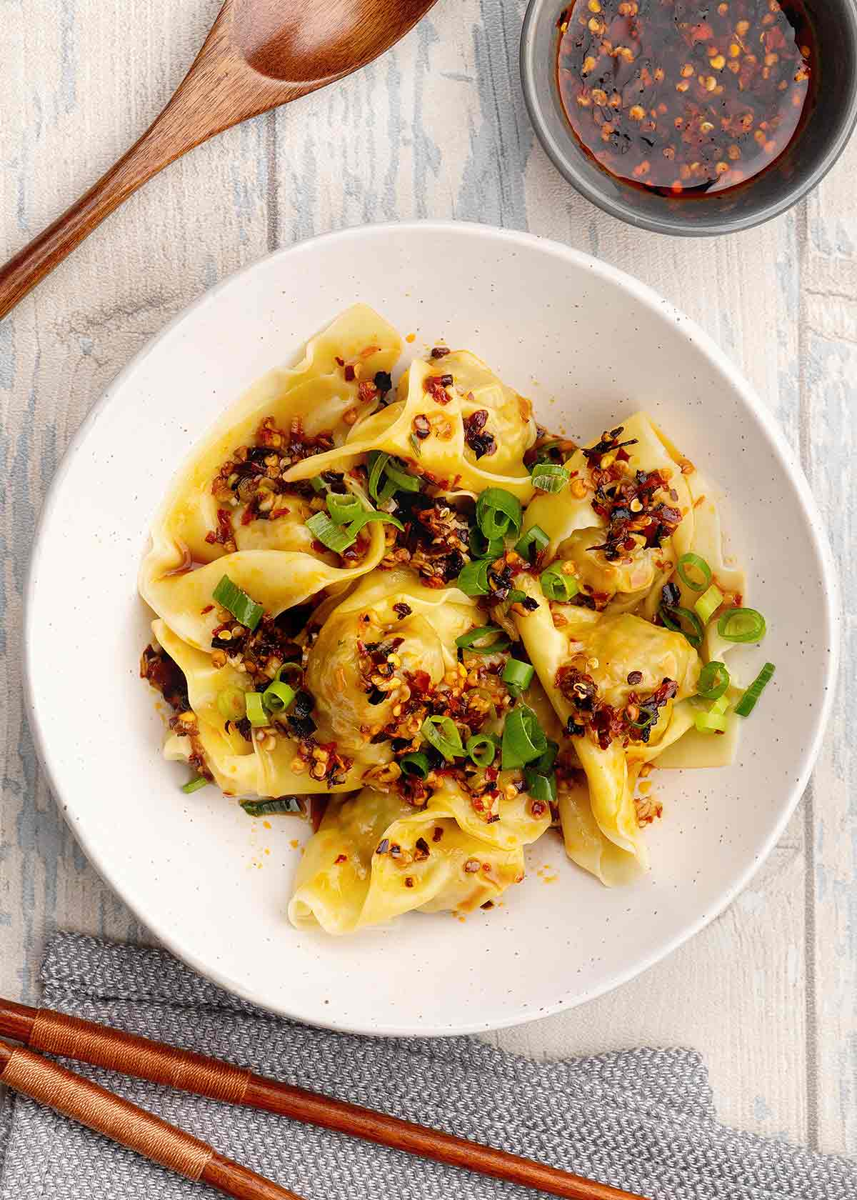 A white bowl containing wontons with chilli oil and spring onions on top.
