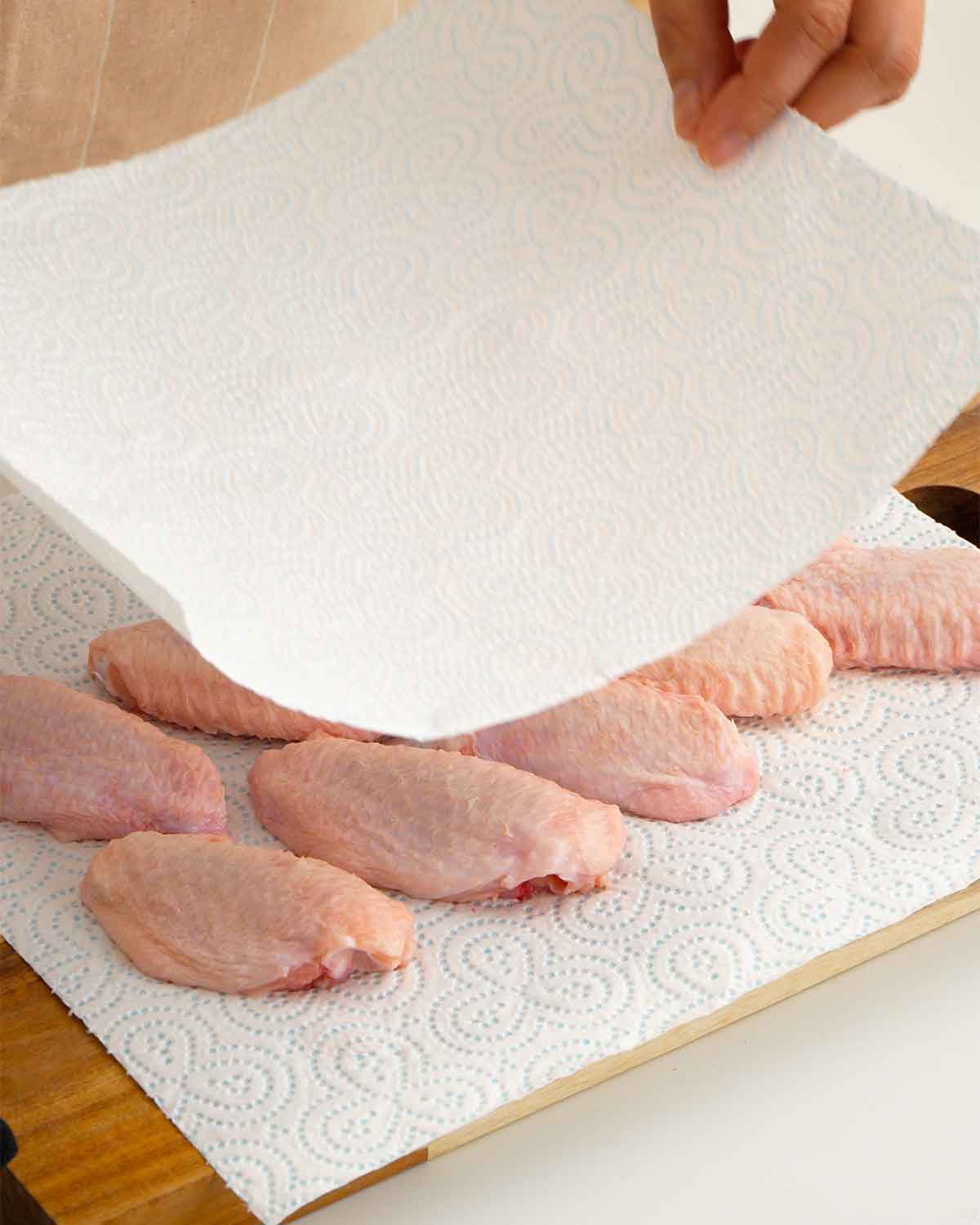 An image showing how to pat dry chicken wings with a white paper towel.