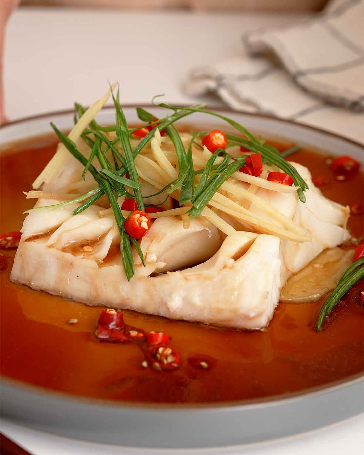 Plating the steamed cod with ginger, green onions, chilli and soy sauce mix.