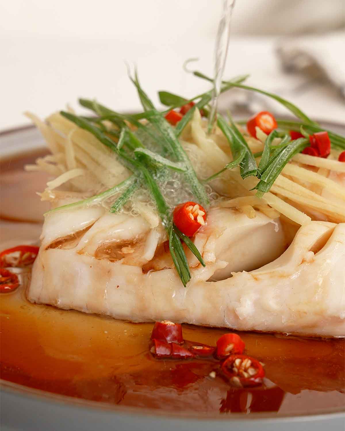 A picture of smoking hot oil is pouring over the fish fillets.