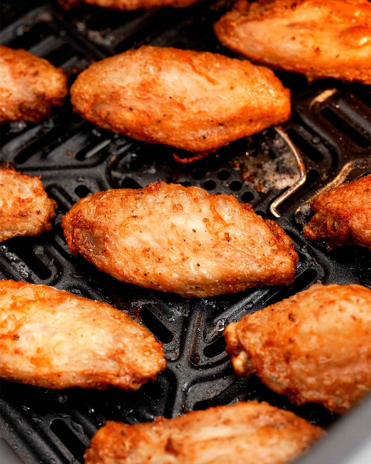 A black air fryer basket containing fried golden colour crispy chicken wings.