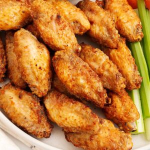 A white plate containing golden colour crispy air fryer chicken wings with green celery sticks on the side.