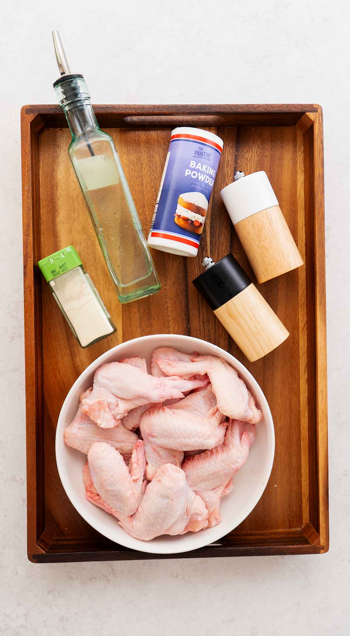 Labelled ingredients of making air fryer chicken wings displayed on the wooden tray.
