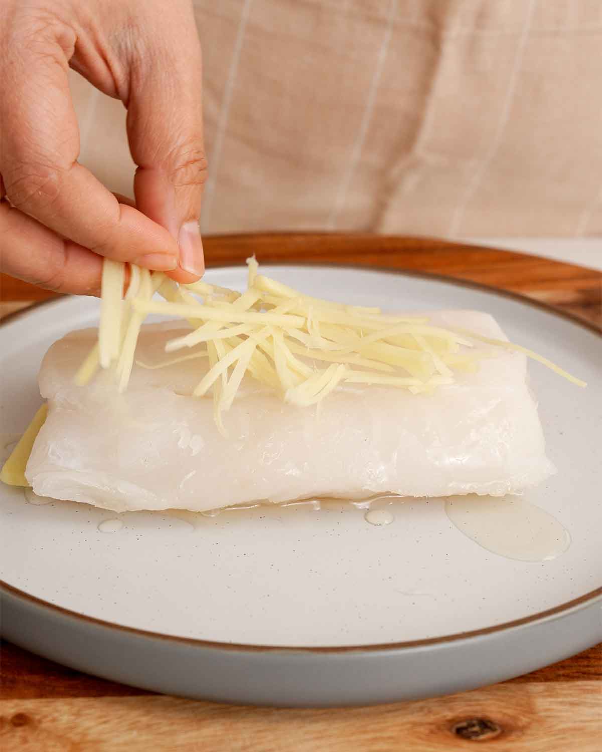 An image showing how to arrange cod fish fillets over the ginger slices and ginger strips.