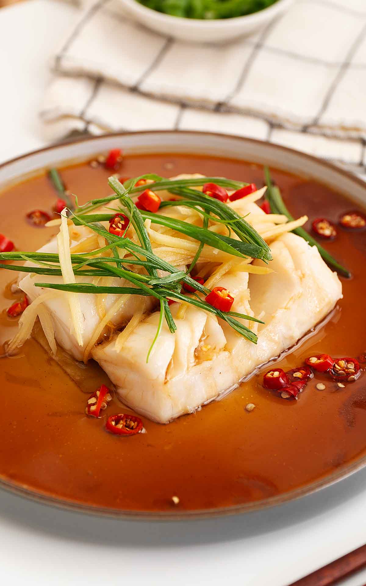 An image of a white flaky cod fish with sauce and fresh herbs in a grey plate.