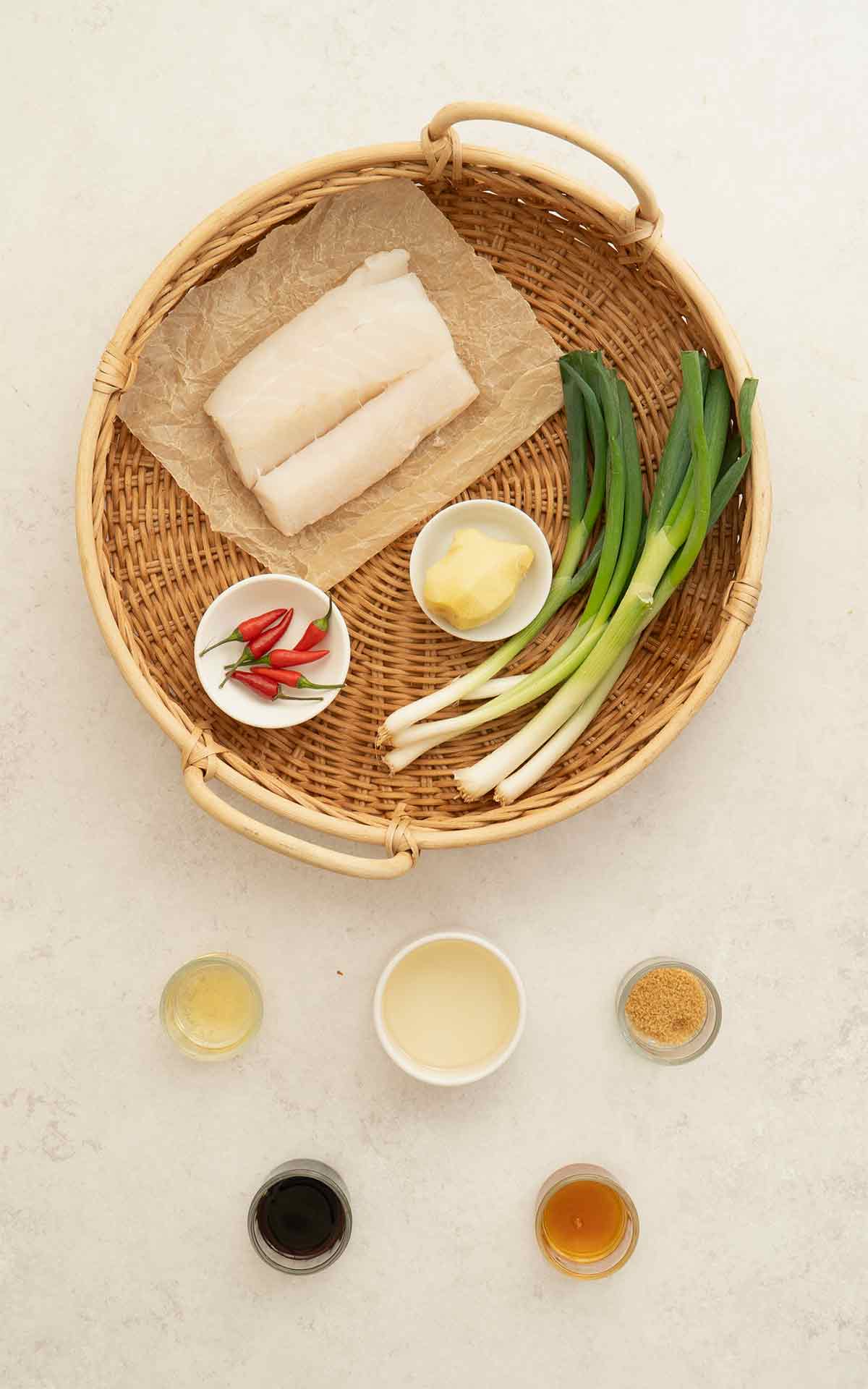Labelled ingredients of making steamed cod fish, displayed on the white table.