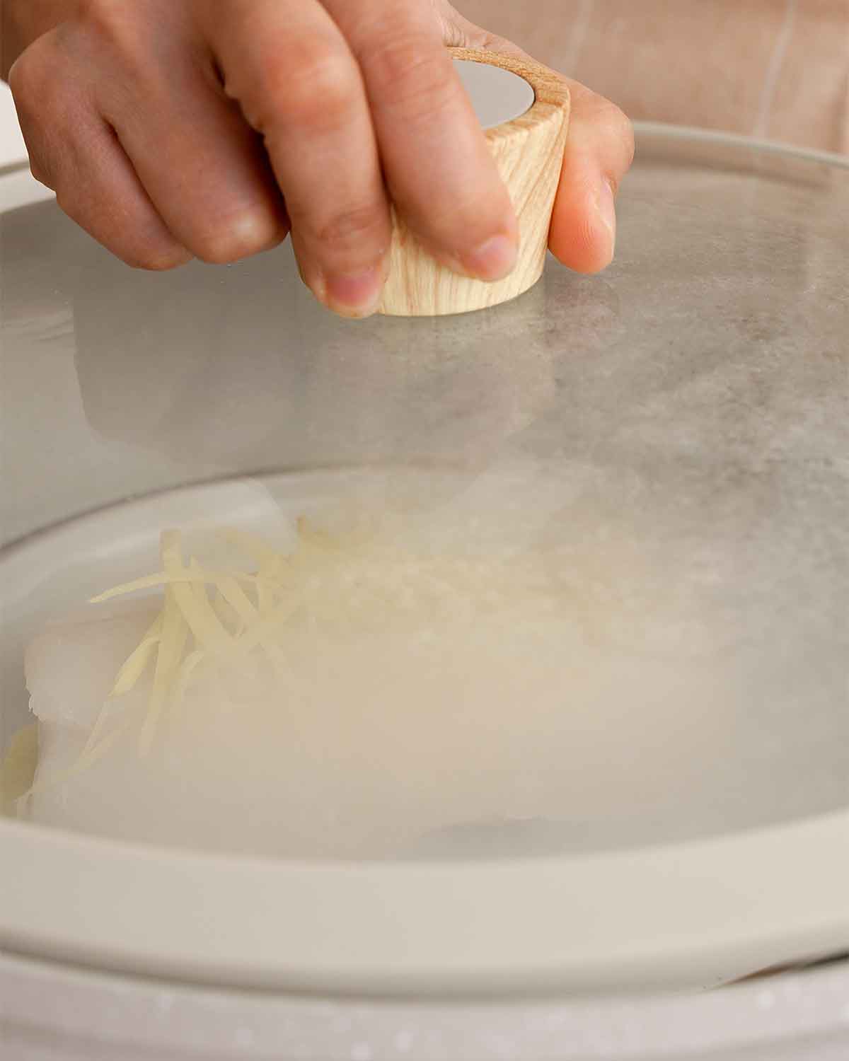 A picture of a large white steaming pot containing cod fish and plate inside.