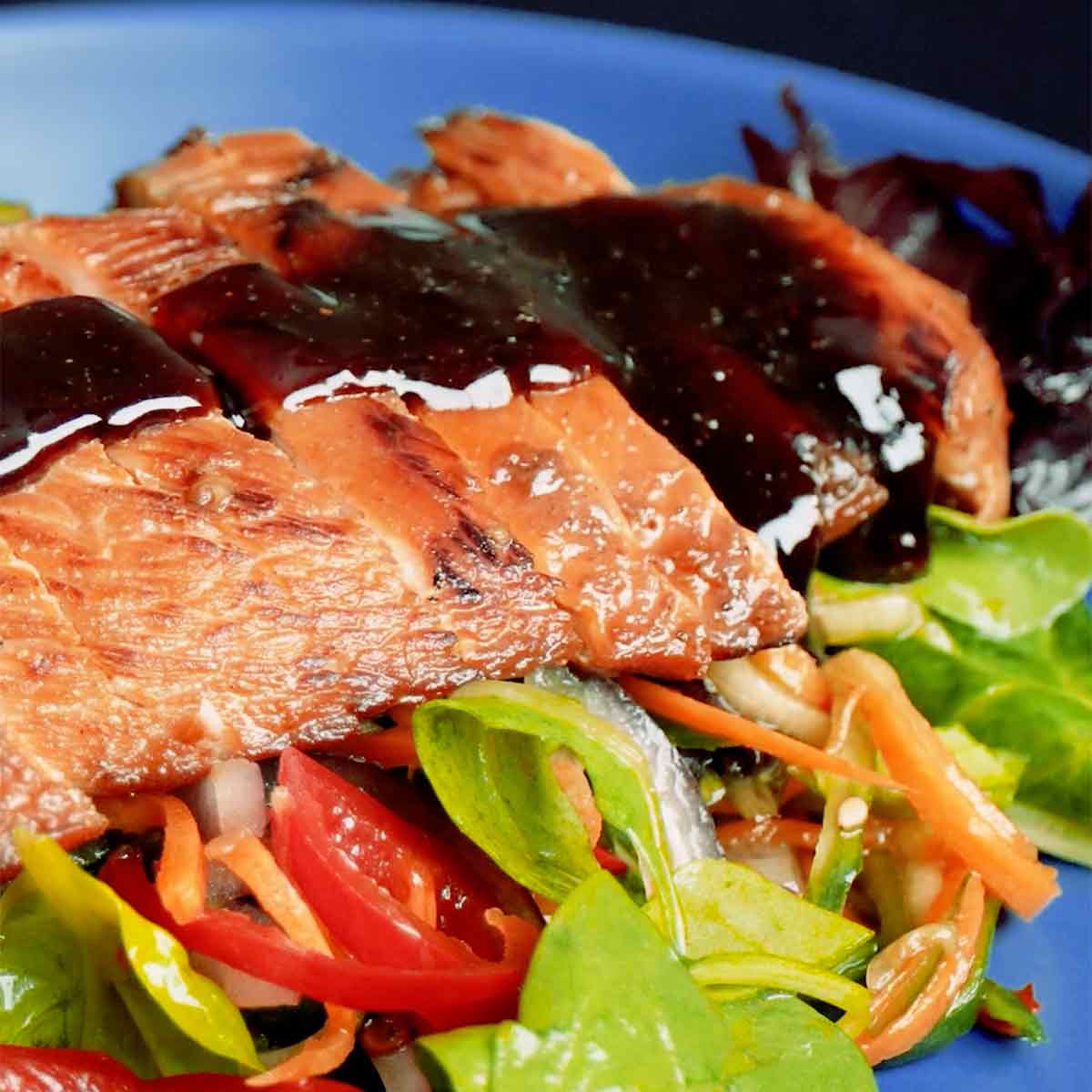 A serving plate containing mixed salad topped with Chinese grilled chicken slices and sauce.