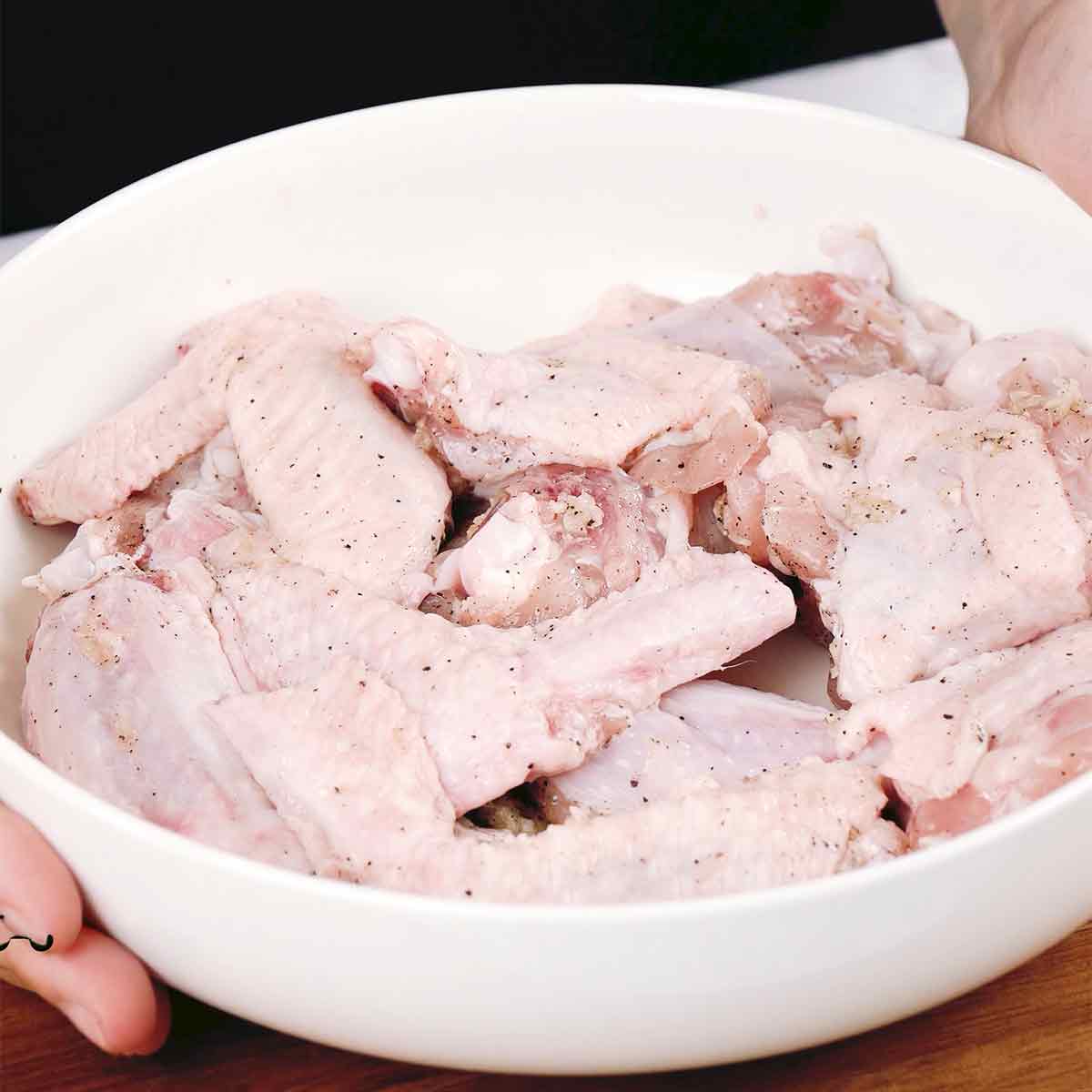 A white bowl containing chicken wings with marinade ingredients.