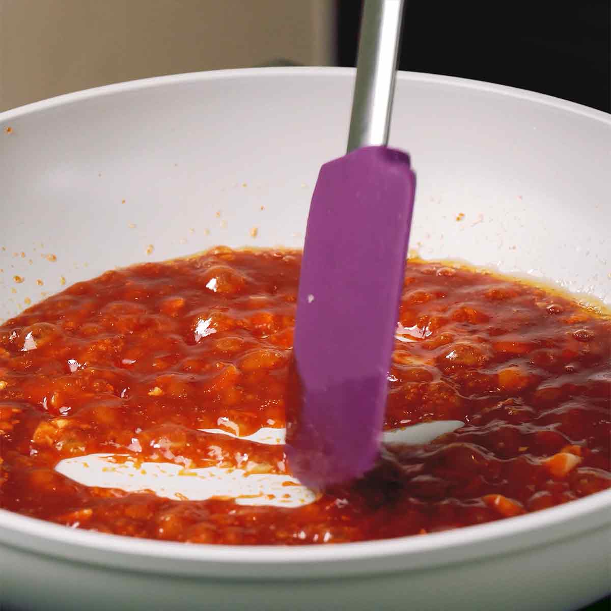 A white pan contains vibrant red colour Korean Chicken Wing sauce.