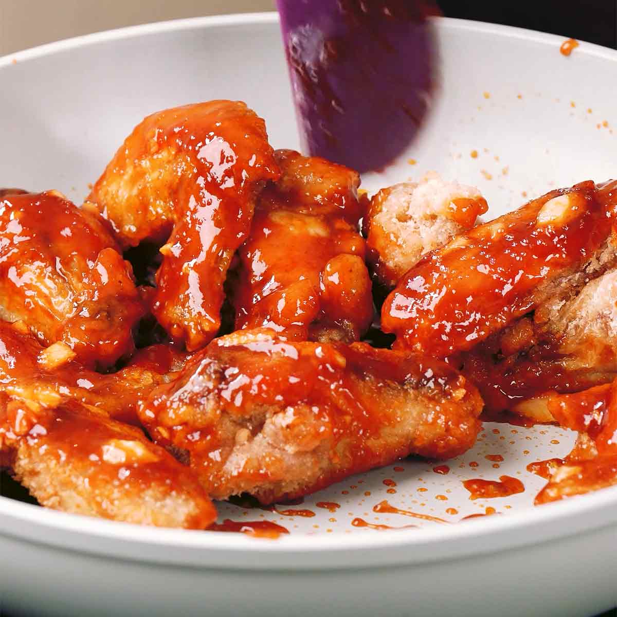 An image showing how to toss fried chicken wings and sauce together.