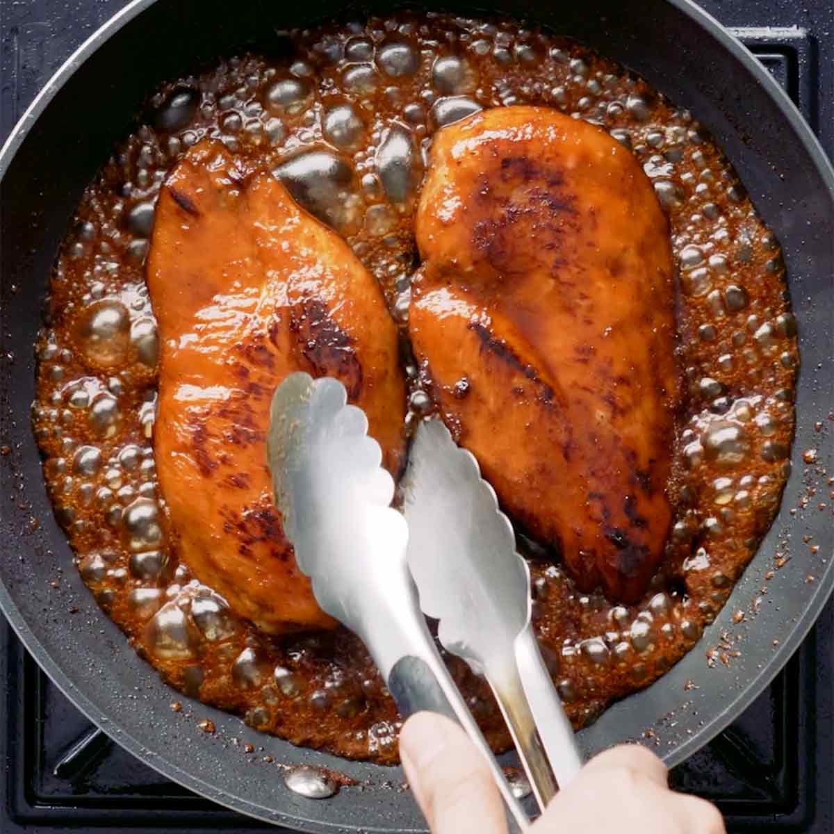 A black skillet pan containing grilled chicken breast fillets with glossy sauce.