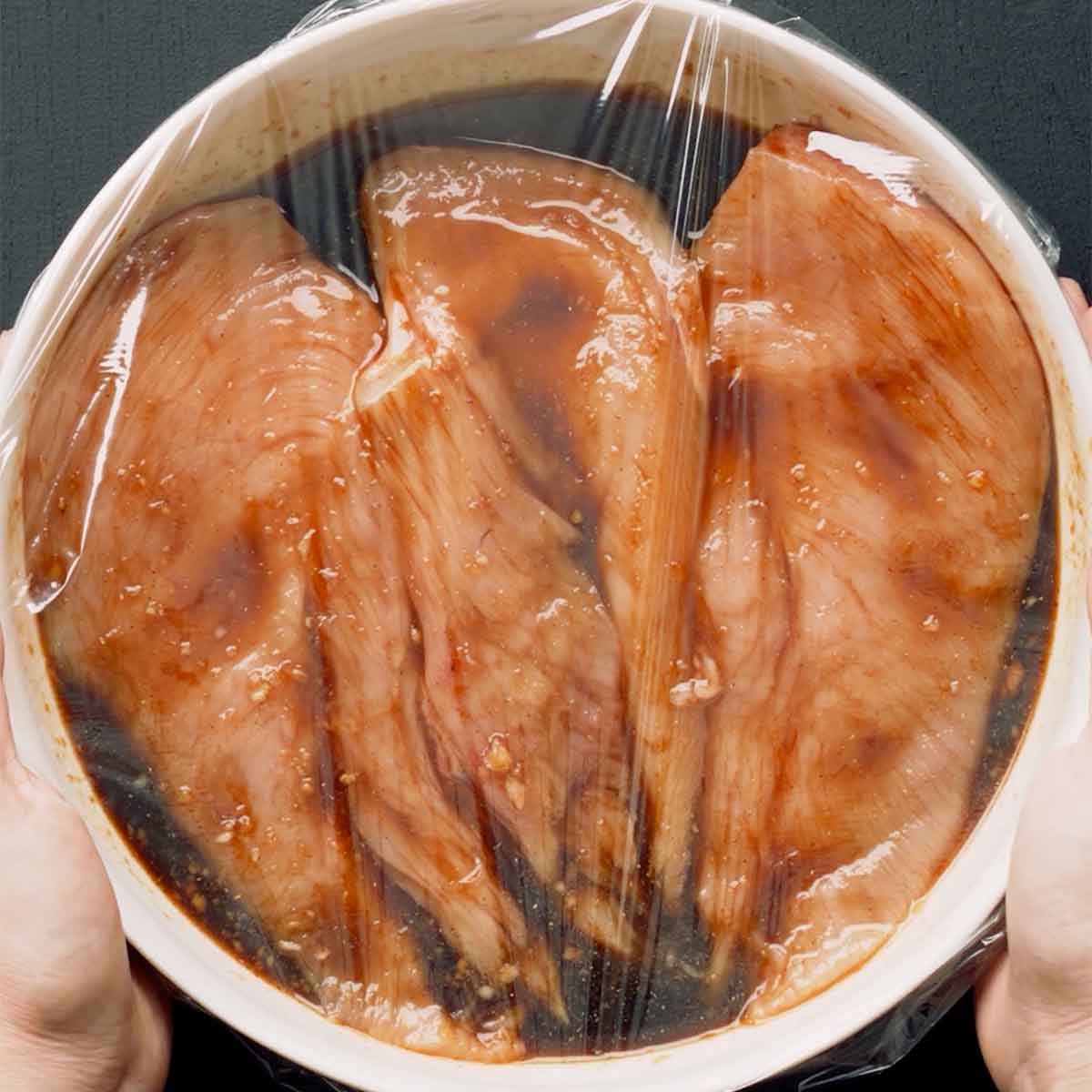 A white bowl containing chicken and marinade sauce.