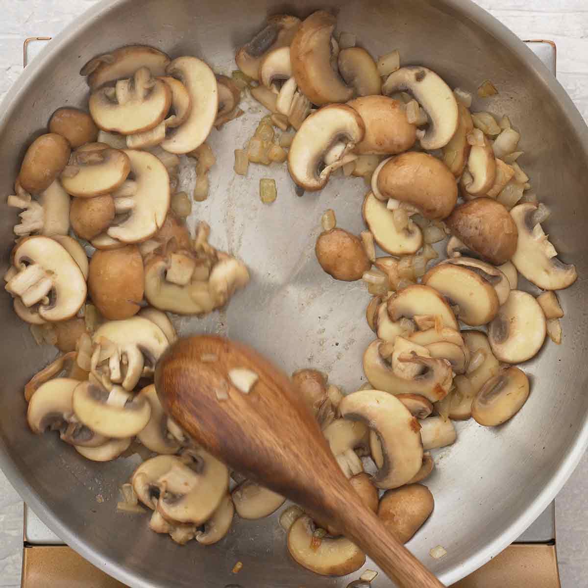 An image showing a large pan containing sauteed onions, garlic, and mushrooms.