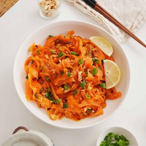 A white bowl containing ribbon texture carrot salad with spring onions and crushed peanuts and sesame seeds on top.