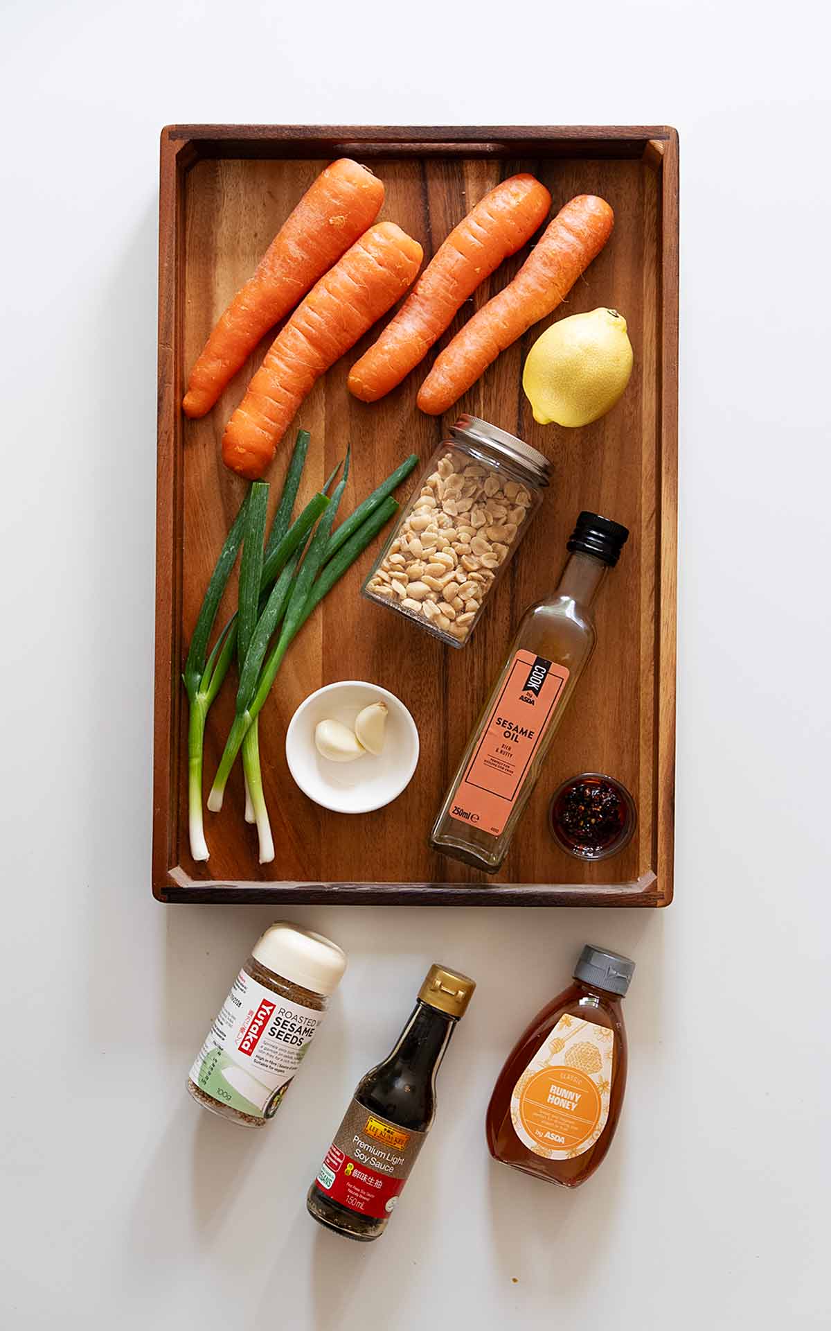 Labelled ingredients of making carrot salad displayed on the wooden tray.