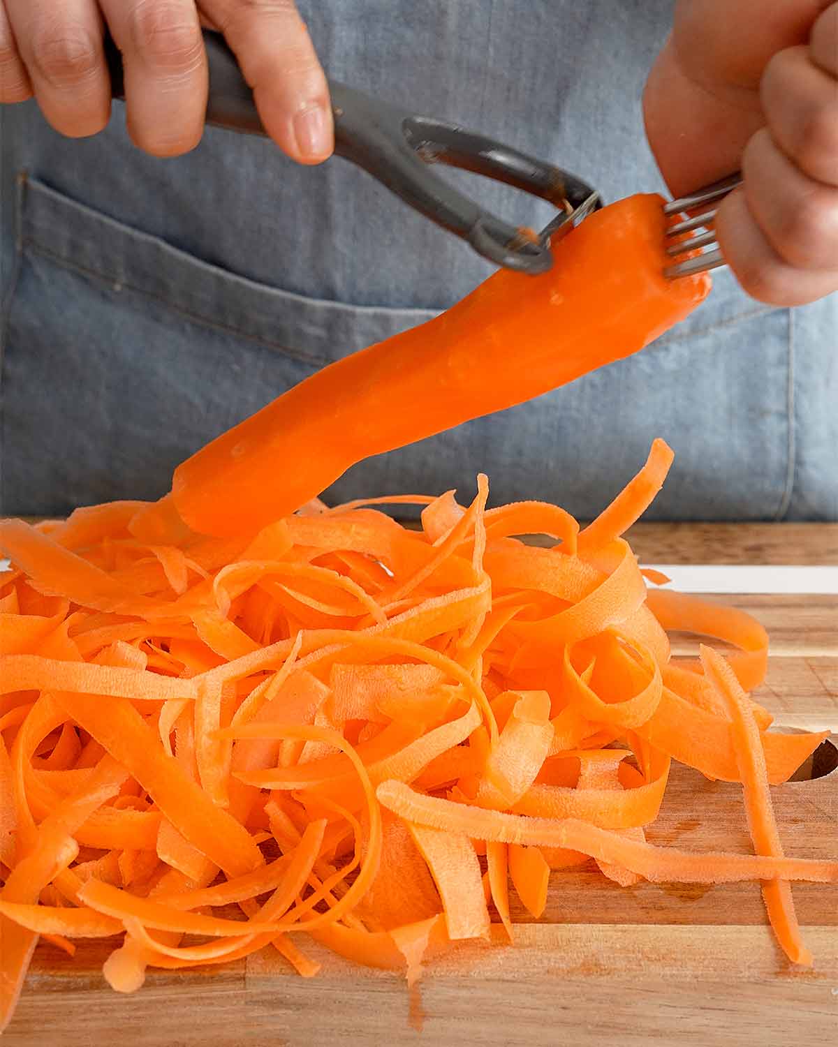 An image showing how to peel carrots into thin ribbons with a vegetable peeler.