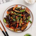 A white plate containing aubergine stir fry with garlic and bell peppers.