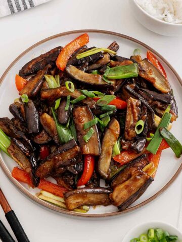 A white plate containing aubergine stir fry with garlic and bell peppers.