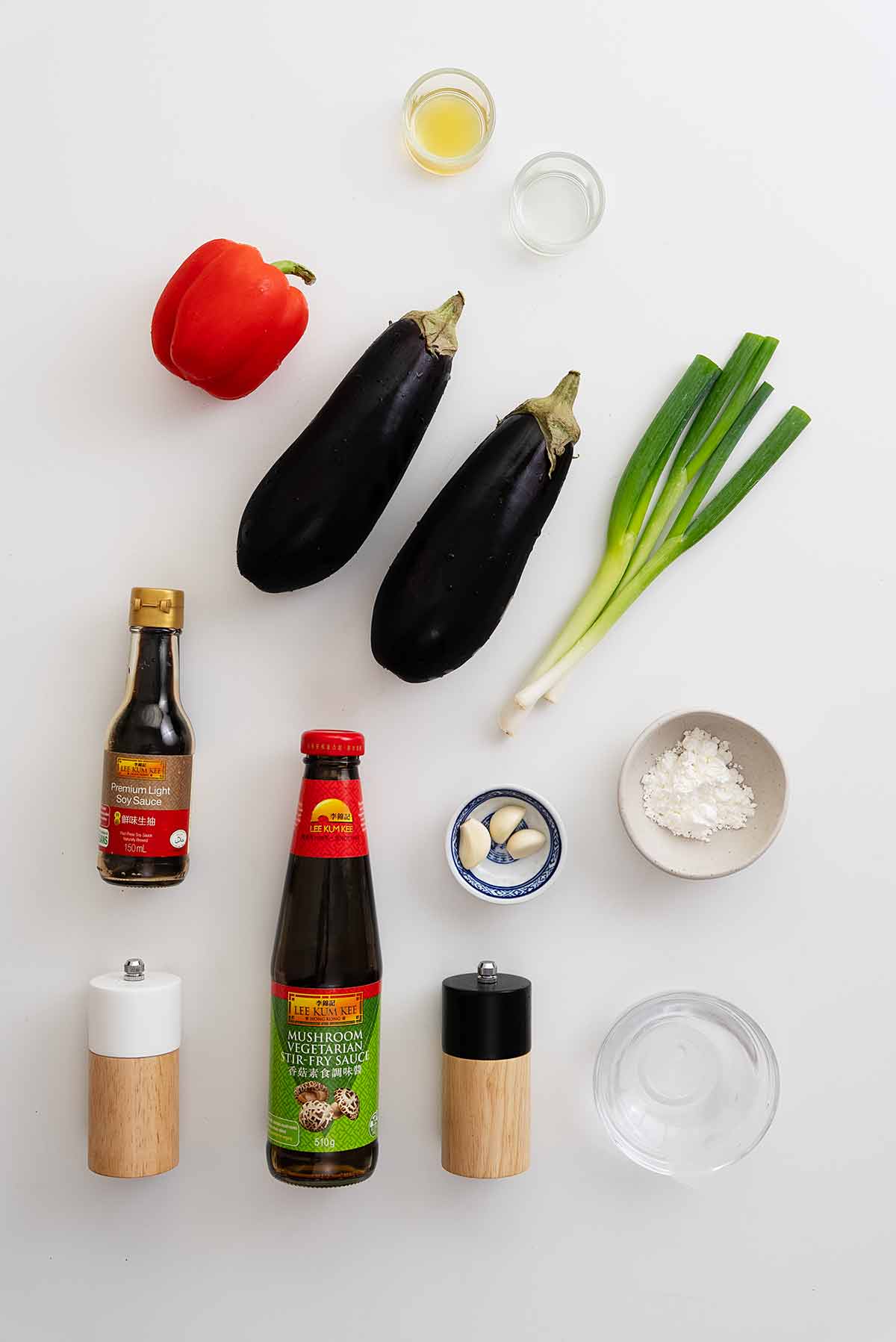 Labelled ingredients of making aubergine stir fry displayed on the white table.