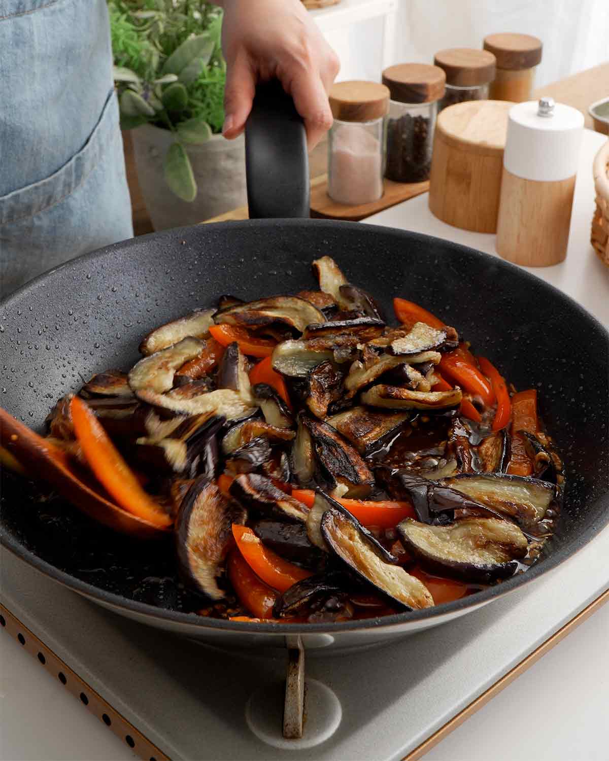 An image showing black non-stick pan containing stir fried aubergine, bell peppers, and sauce.