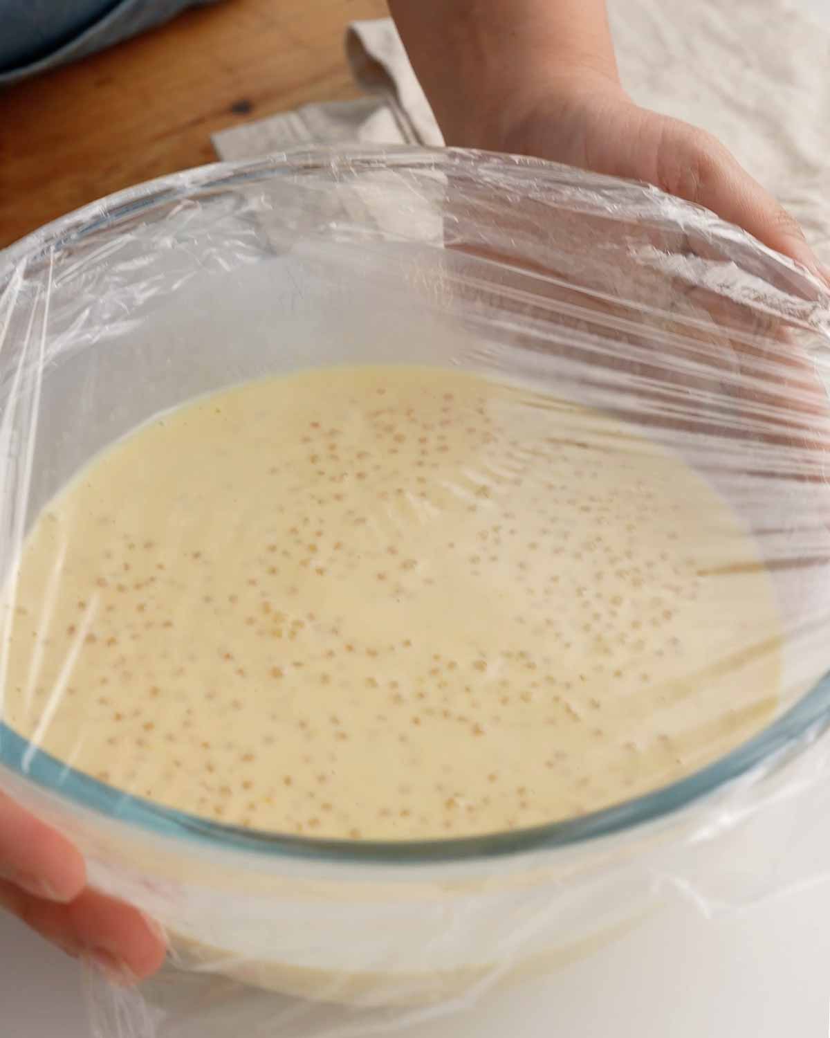 An image of a large glass bowl containing a sago mango drink, covered with a cling film.