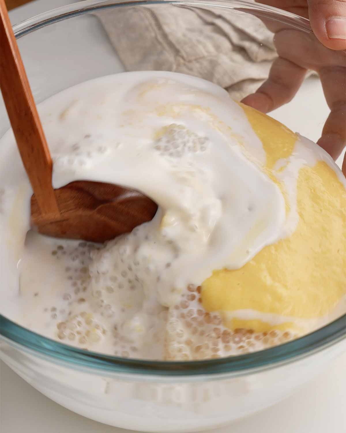An image showing combining the mango puree, sago and coconut milk in a large mixing bowl.