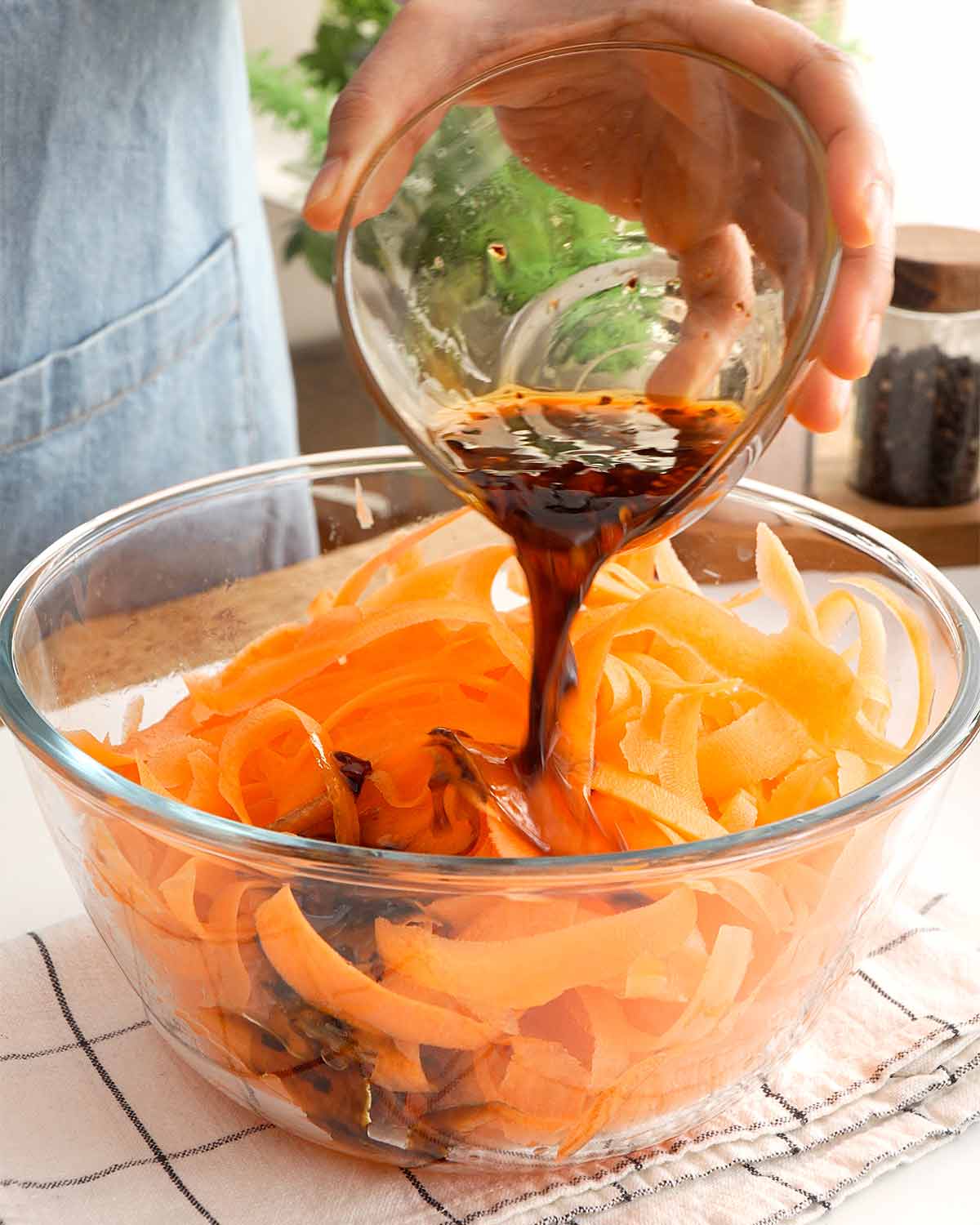 An image of a salad bowl containing carrot ribbons and a hand pouring a sauce over it.