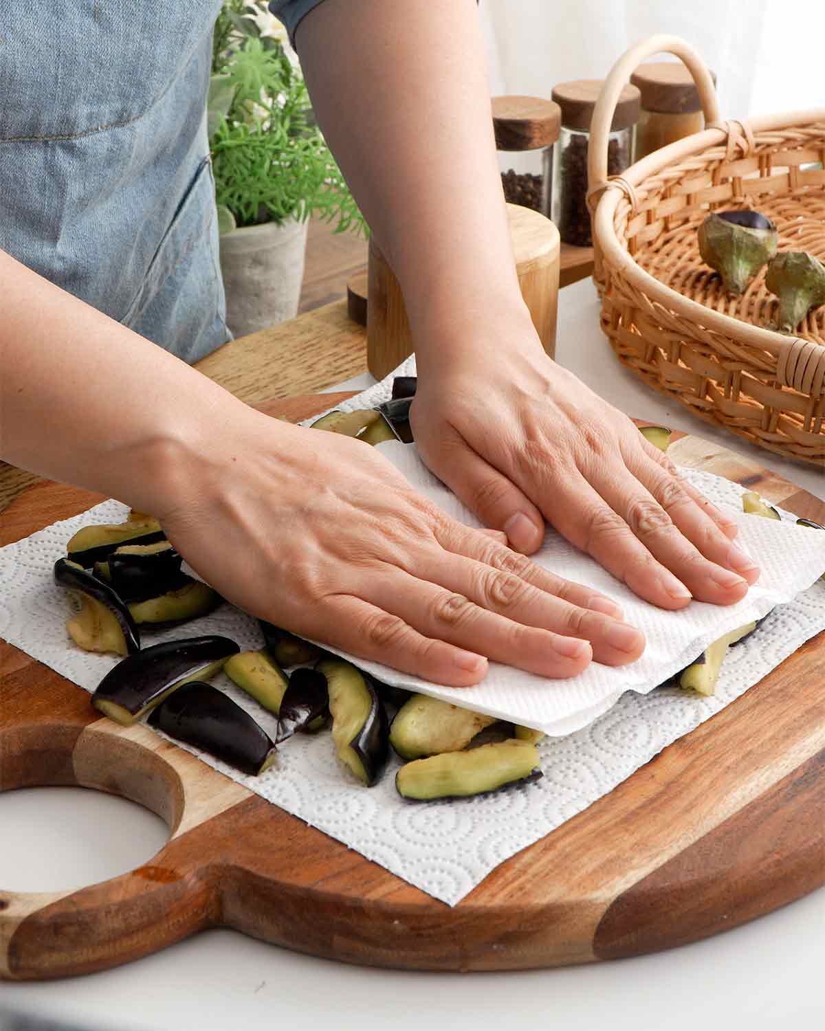 An image showing how to dry aubergine on the wooden chopping board with a paper towel.