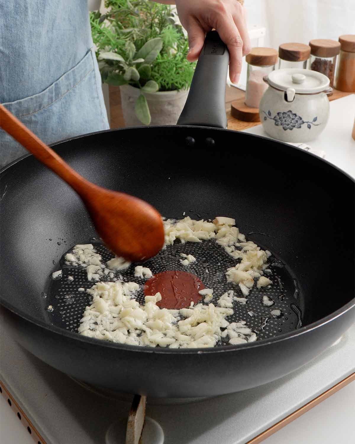 An image showing how to saute garlic in a large black wok.