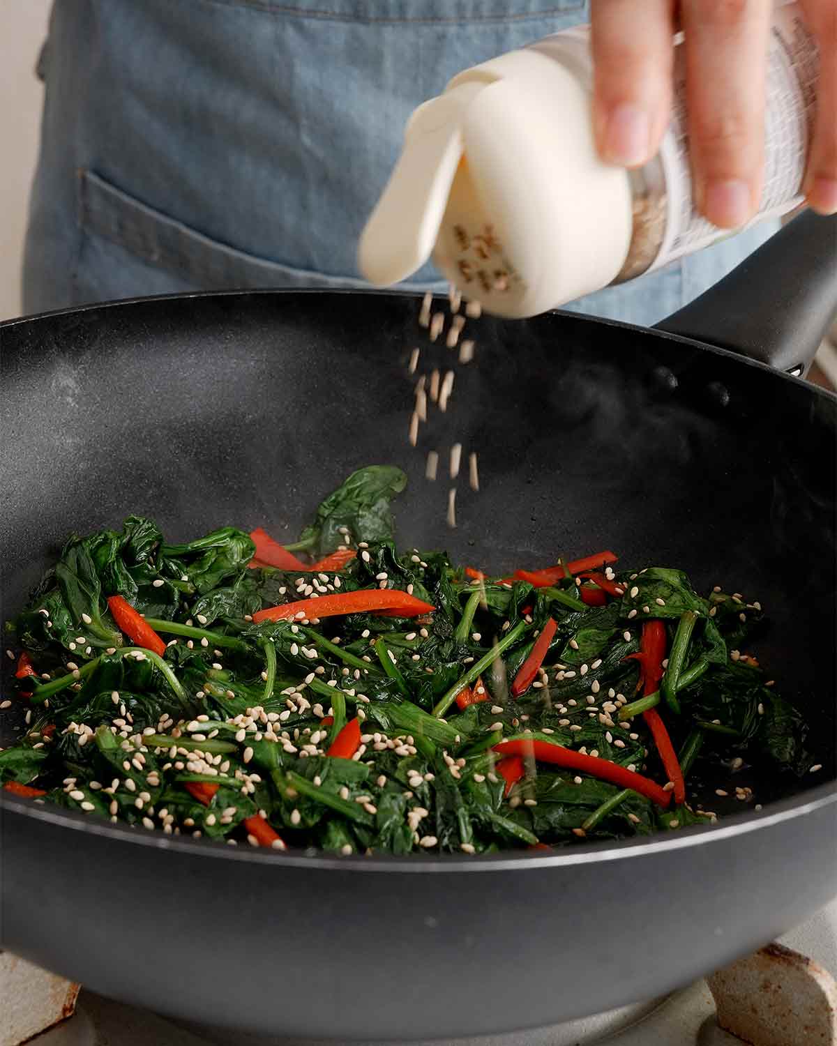 Finishing the dish with sesame oil and sprinkling sesame seeds.
