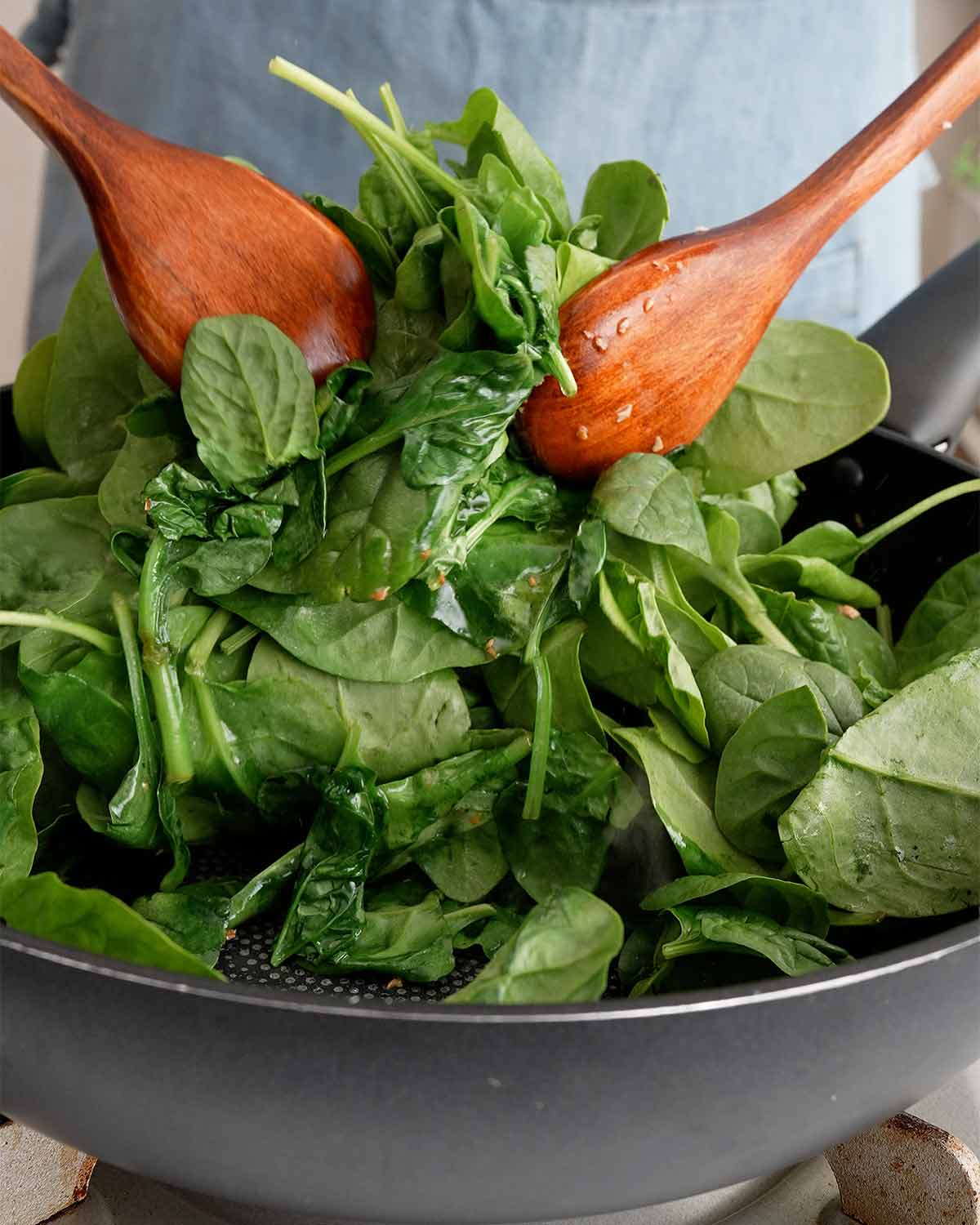 An image showing how to toss spinach in a large wok.
