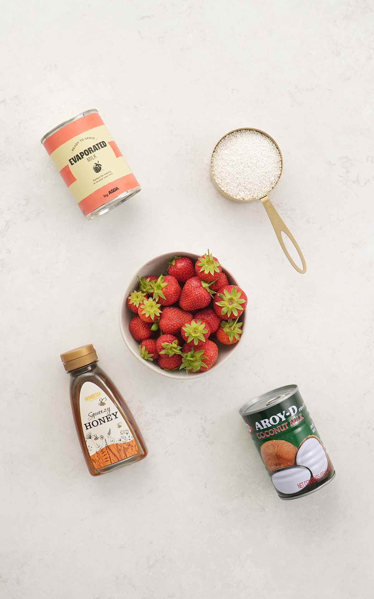 Labelled ingredients making sago and strawberry drink displayed on the white table.